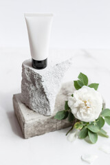 White tube of cream or body lotion, on a piece of stone on a natural white background with white flower, rose. Organic cosmetic. Treatment spa beauty skincare. Healthcare and medicine. Mock up