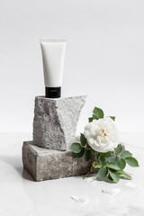 Fototapeta na wymiar White tube of cream or body lotion, on a piece of stone on a natural white background with white flower, rose. Organic cosmetic. Treatment spa beauty skincare. Healthcare and medicine. Mock up