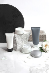 Mock up. Jar and tubes of cream or body lotion, white and gray, on a pieces of stone on a white background with flower, rose. Natural cosmetics. Treatment spa beauty skincare. Healthcare, medicine