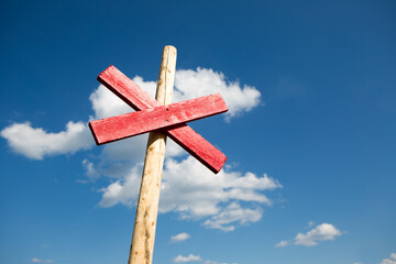 Red railway crossing sign made of wood with blue cloudy sky background.