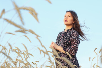 Beautiful woman looking into the distance while standing in a wheat field on a background of blue...