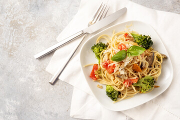 Spaghetti with tomatoes, broccoli, bell pepper, eggplant and herb garnish, healthy vegetarian pasta meal on a white plate and a light rustic background, copy space, high angle view from above
