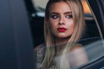 Plakat Luxury rich sexy woman with evening make up sitting in a car and looking through window. She ready for a party. Evening portrait.