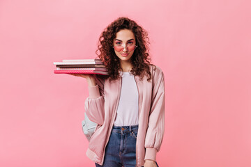 Self confident girl in fashion daily outfit holding books on pink background