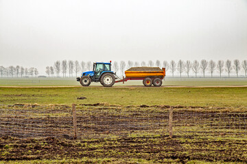 Tractor with tipper trailers transports a load of sand over a polder dike; Netherlands.  