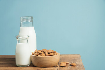 Bottles of fresh milk with almonds on wooden table on light blue background.