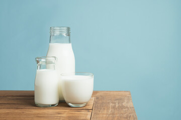 Bottles of fresh milk on wooden table on light blue background.