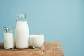 Bottles of fresh milk on wooden table on light blue background.