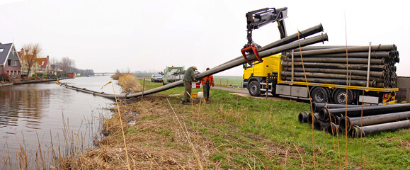 Technicians disassembling a pipeline. A truck-mounted crane pulls the pipe from a canal, while two others unscrew the pipe sections.