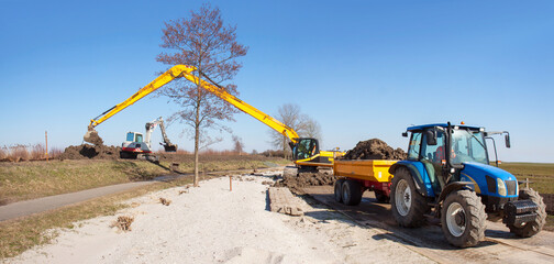 Dike reenforcement in The Netherlands: a tractor with tipper trailer brings clay, a large crane...