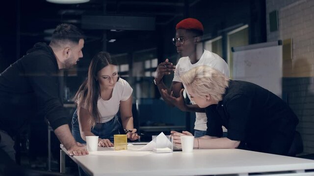 Multi-ethnic team of young creative people have a vigorous business discussion in the meeting room. African American businessman colleague actively gesticulates while talking.