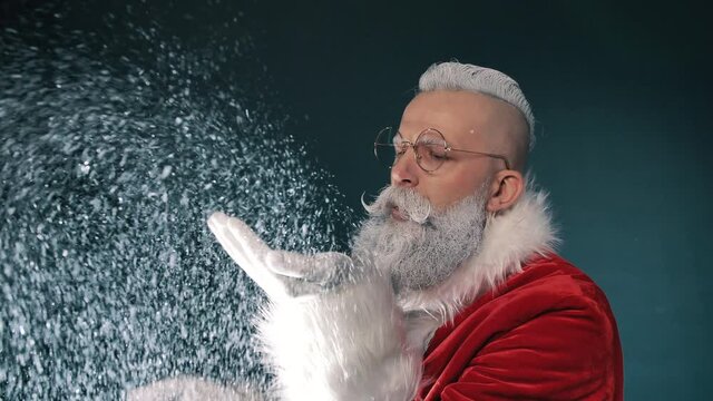 Crazy comic hipster Santa Claus tastes snow, blows him off hands, silly humor fantasy jokes for holiday mood closeup indoors. Funny winter control, quality checking for happy New Year, merry Christmas