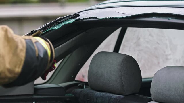 Firefighter beraking glass on car window extricate trapped victim from the car. High quality 4k footage