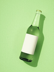 One closed transparent glass beer bottle laying on light green surface.