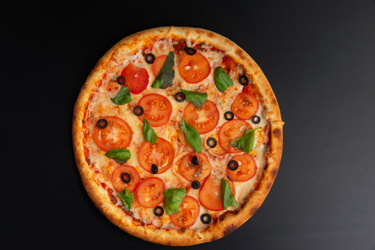 homemade pizza with tomatoes and herbs on a dark background