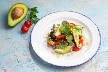 salad with avocado, tomatoes and herbs in a plate on a gray background