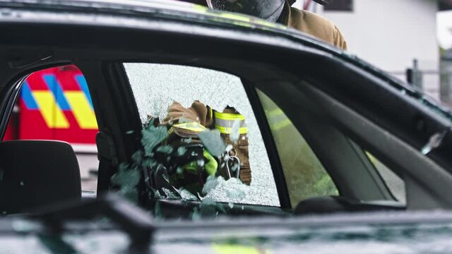 Firefighter beraking glass using jaws of life to extricate trapped victim from the car. High quality 4k footage