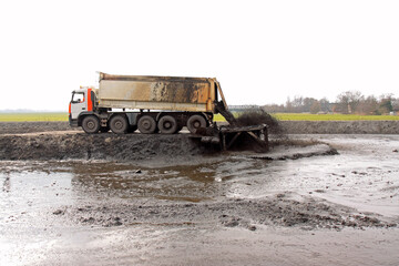 Large truck with tipper trailer unloads its freight of dredging spoil (sludge, sediment) into a storage compartment (depot)