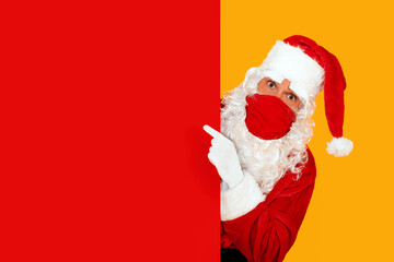 astonished santa claus wearing a red face mask pointing to a red blank space