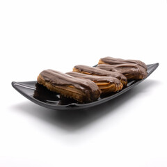 Five chocolate-coated eclairs on a rectangular black platter. Confectionery  lie in a row. Angle view. Isolated over white background.