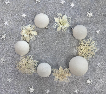 Christmas decoration. White balls, white openwork flowers, snowflakes on silver gray glitter background with space for text. Top view, flat lay