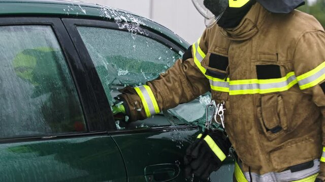 Firefighter beraking glass on car window extricate trapped victim from the car. High quality 4k footage