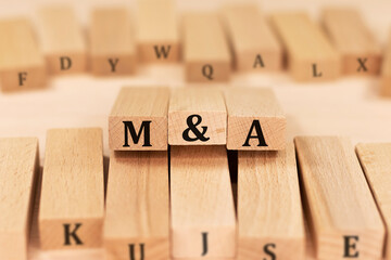 Word M and A Merger and Acquisition on wooden blocks beige background top view, scattered cubes around random letters