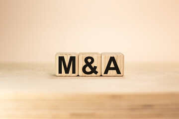 Word M and A Merger and Acquisition wooden blocks beige background top view