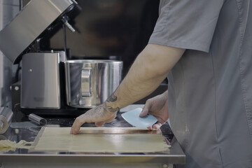 Closeup of unrecognizable male pastry chef with tattoos slices dough with silicone cutter. Male hands preparing dessert on commercial kitchen