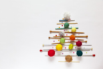 Merry Christmas and Happy New Year: funny Christmas tree made of knitting accessories, woolen balls, knitting needles and crochet hooks on a white background. Copy space, flat lay, mock up, top view