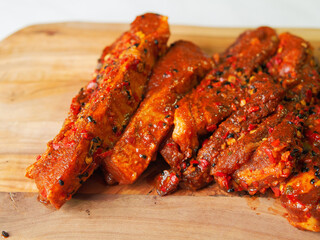 Raw uncooked fresh pork belly slices on a wooden cutting board. Red meat marinade with oil and herbs,