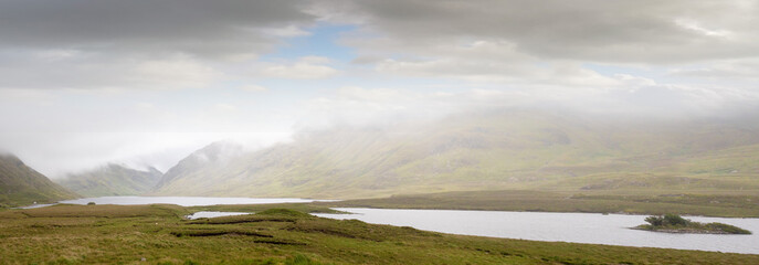 Landscape view on a lake shore in Connemara mountains in a mist and low clouds, Ireland. Panorama image. Nobody. Beautiful surreal atmosphere
