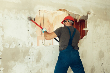 builder with a hammer in his hands breaks the cement wall The builder is dressed in a protective...