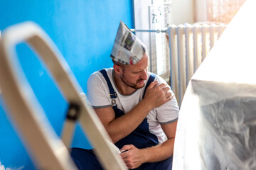 Shot of exhausted painter suffering from pain in his shoulder after working hard isolated on bright background. Portrait of a man at work suffering from shoulder pain. Stressed man holding shoulder.
