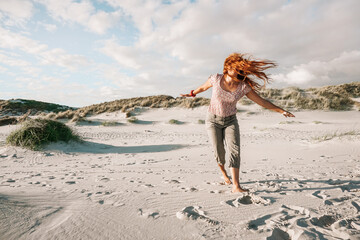 Junge Frau tanz mit fliegenden kupferfarbenen Haaren am Strand von Amrum