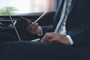 Businessman using smartphone and working on laptop computer inside a car during going to office