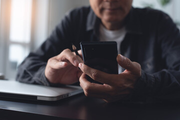 Casual asian business man using mobile phone during working on laptop computer in office