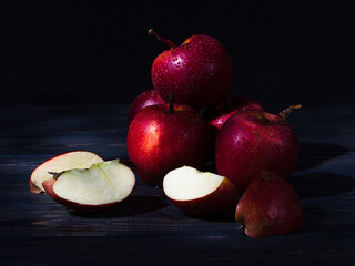 Whole red apples and a sliced apple with water drops on a dark wooden background. Close up. 