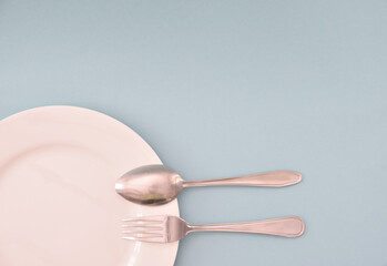 A table spoon and fork lying side by side and resting at one end on a white porcelain plate.