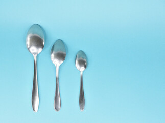 Three spoons laid out parallel to the bottom up and isolated on a light blue background.