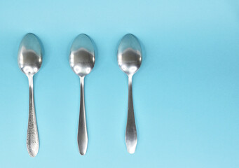 Three tablespoons lying in a row upside down on a light background.