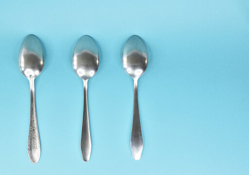 Three tablespoons lying in a row upside down on a light background.