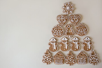 Homemade gingerbread cookies in  shape of  heart,  snowman,  house,  star,  ball are laid out in  shape of  Christmas tree. Small colorful candies decorate  tree. Nearby space for text. festive mood