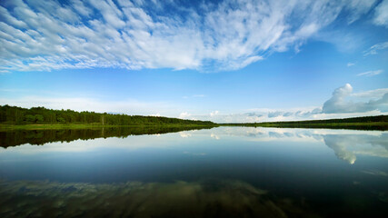 River landscape. Green banks and white clouds are reflected in the mirror of the water.