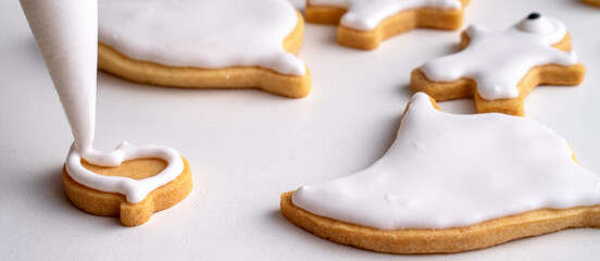 Close up of decorating cute Halloween cookies with frosting in icing bag.