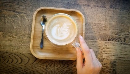 hand with a cup of latte on wooden background