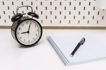  notebook with a black alarm clock and a pen on a white background.