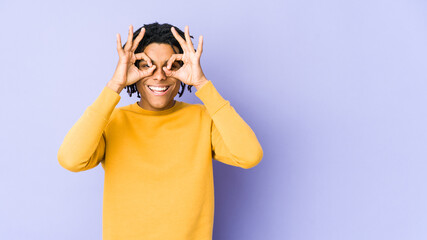 Young black man wearing rasta hairstyle excited keeping ok gesture on eye.