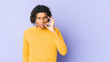 Young black man wearing rasta hairstyle with fingers on lips keeping a secret.