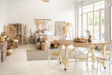 Large spacious room with a trendy loft design of sitting area. huge windows and stylish wicker light furniture inside. an abundance of ethnic decor